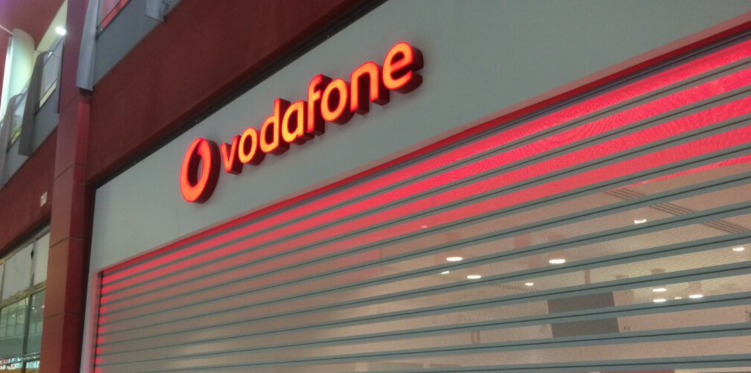 Vodafone storefront with illuminated red signage and security roller shutter
