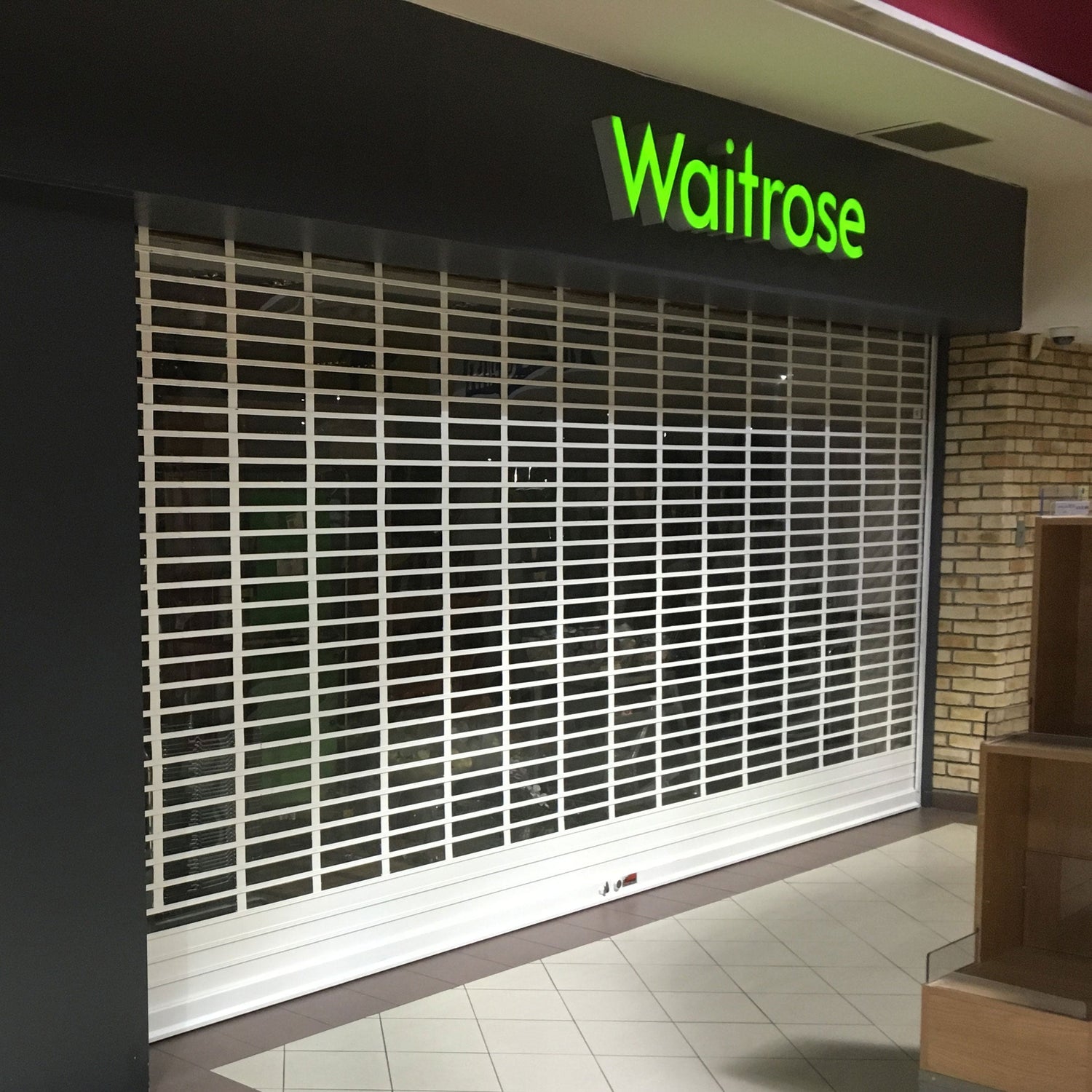 White security roller shutter installed at Waitrose store entrance, featuring grid design for retail protection.