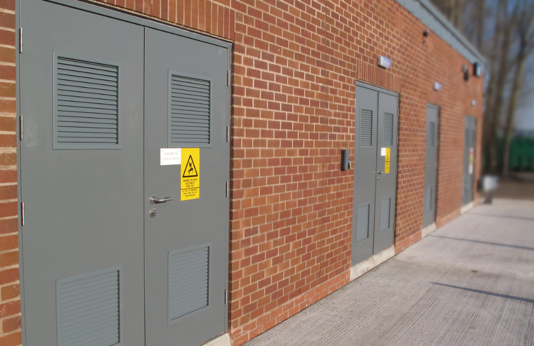 Grey security doors with warning labels on brick building exterior, industrial access control