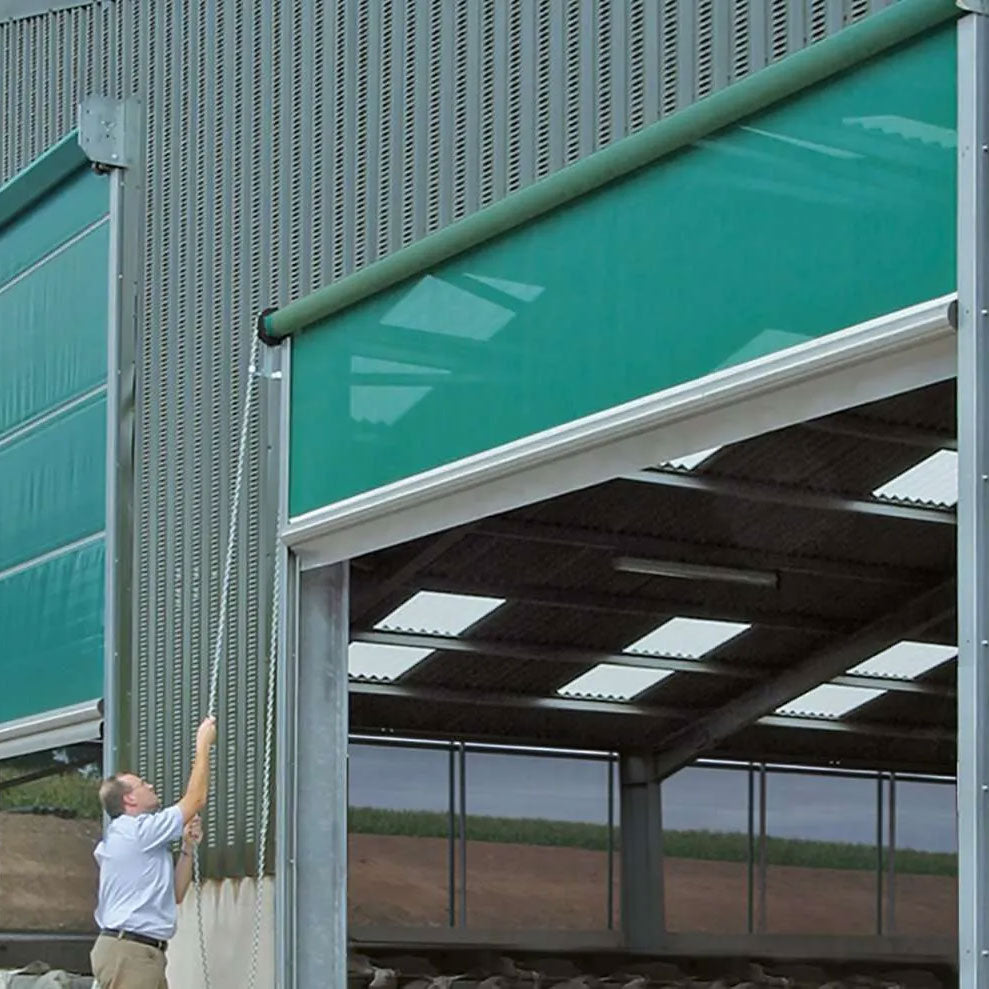 Man operating a green industrial roller shutter door on a metal warehouse building.