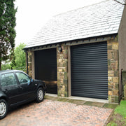 Black automatic roller shutter doors installed on a stone garage building.