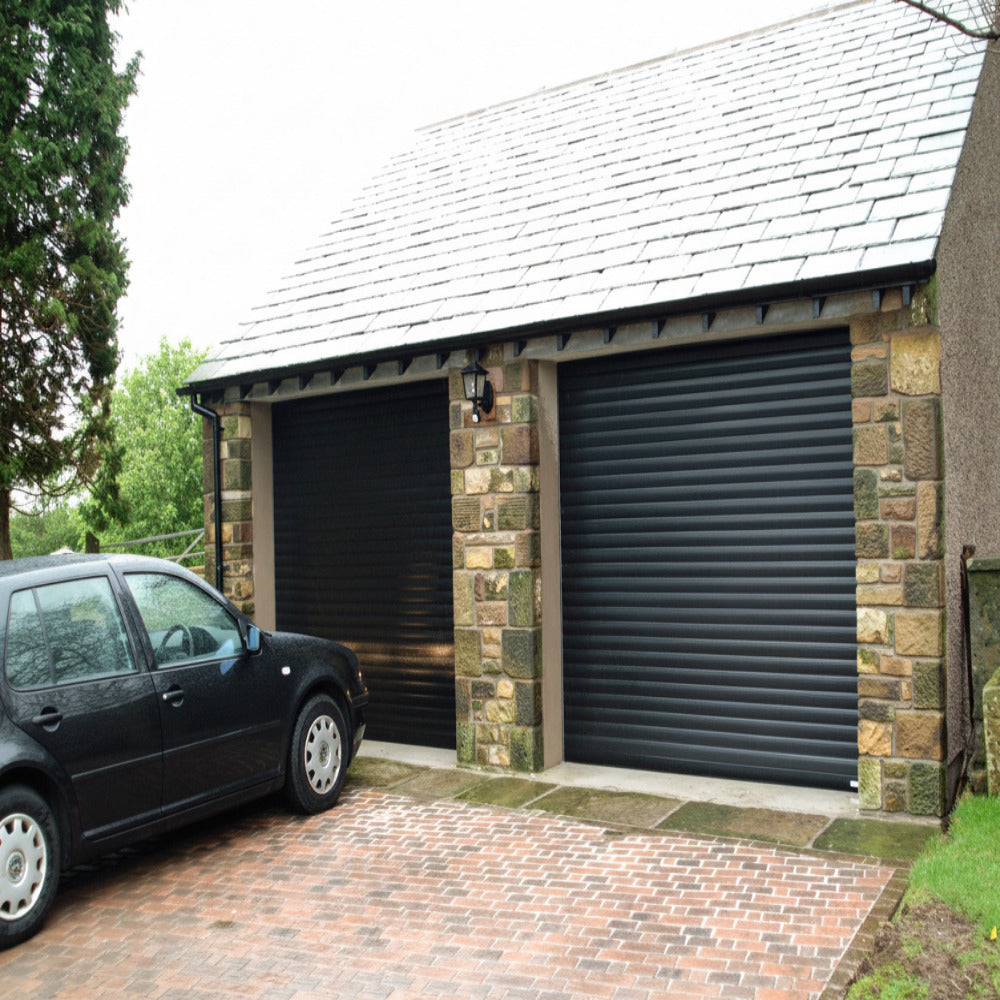 Black automatic roller shutter doors installed on a stone garage building.