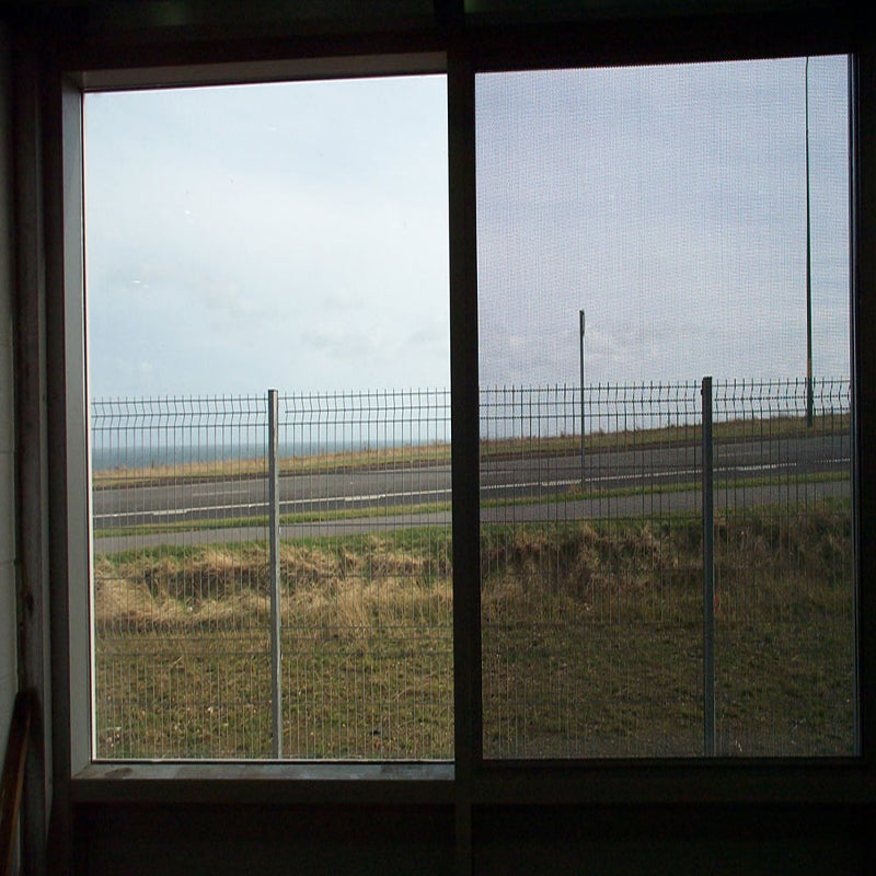 CrimeShield perforated window security mesh installed in a window frame overlooking a road.
