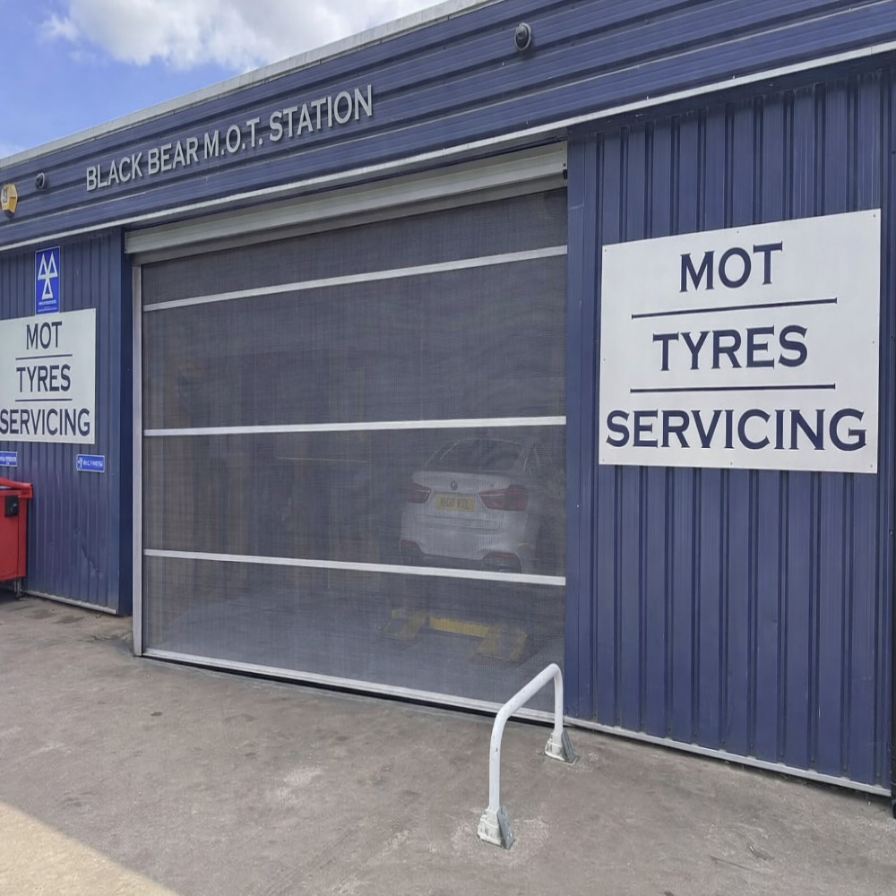 Blue industrial building with a transparent roller shutter door for an MOT and tyre service station.