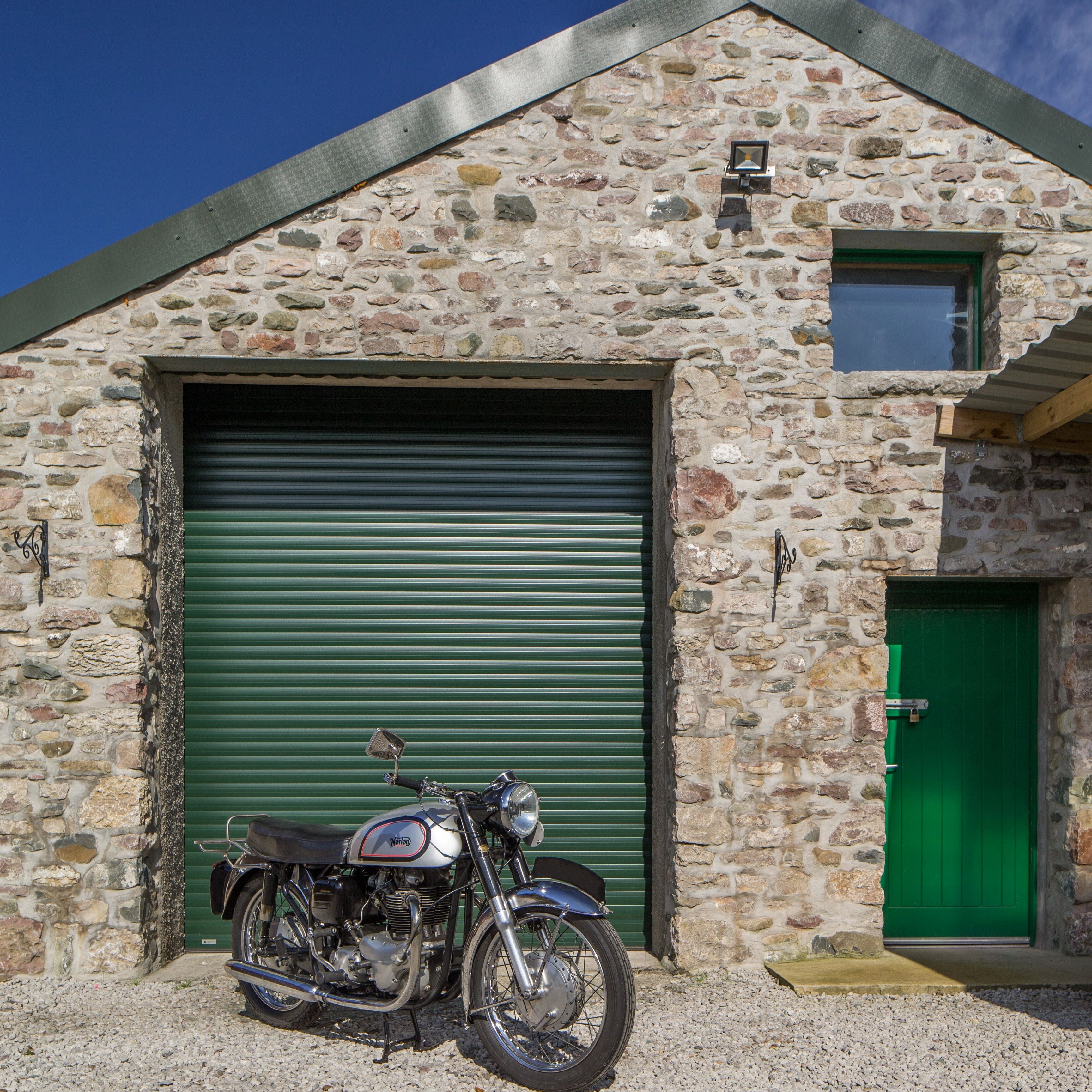 Motorcycle parked in front of a stone building with green doors.