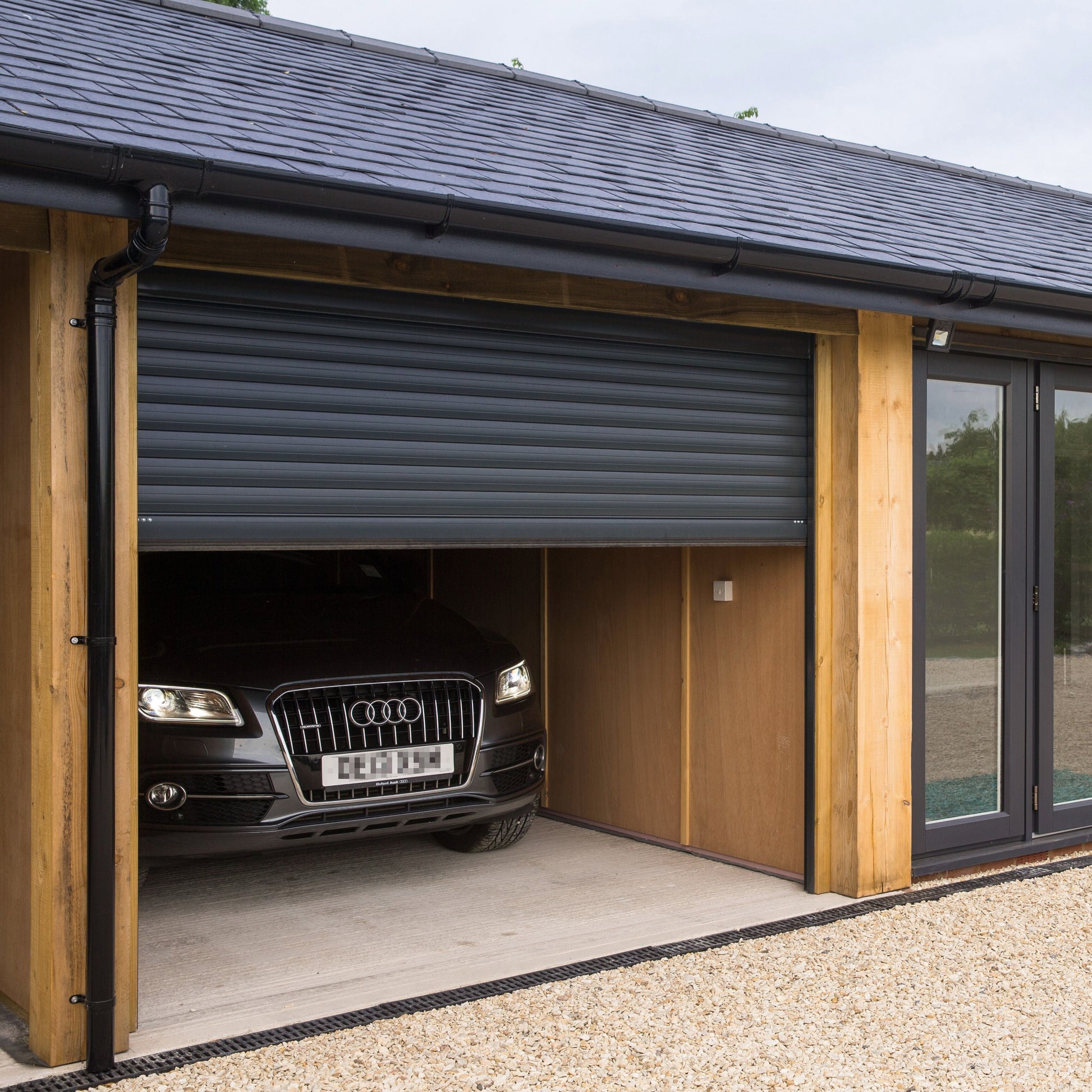 Garage with a black Audi car inside, wooden exterior, and glass door.