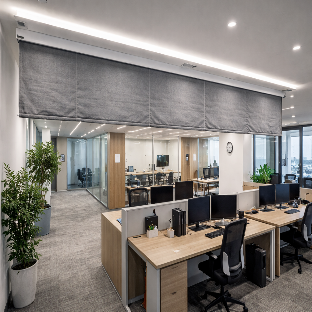 Modern office interior with grey fabric roller blinds and open plan workstations.