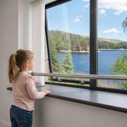 Child looking out window with safety rail, overlooking lake and forest view