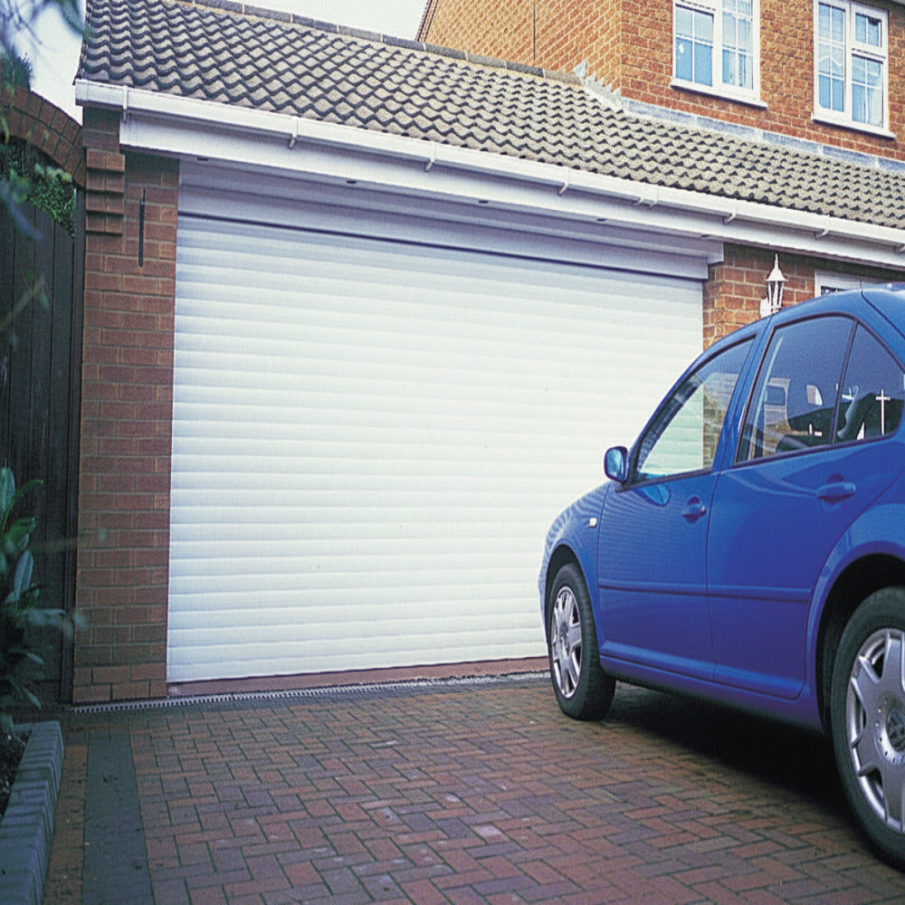 White automatic roller garage door installed on a brick house with a blue car parked outside.