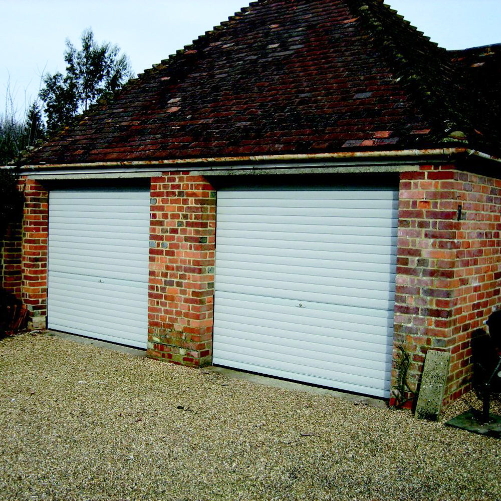 Two light grey roller shutter garage doors installed on a red brick building.