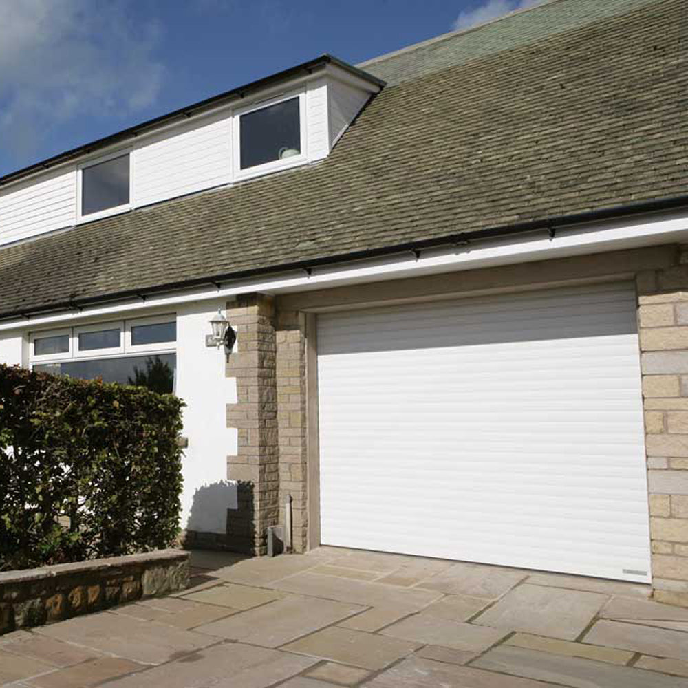 White roller shutter door installed on a stone garage in a residential setting.