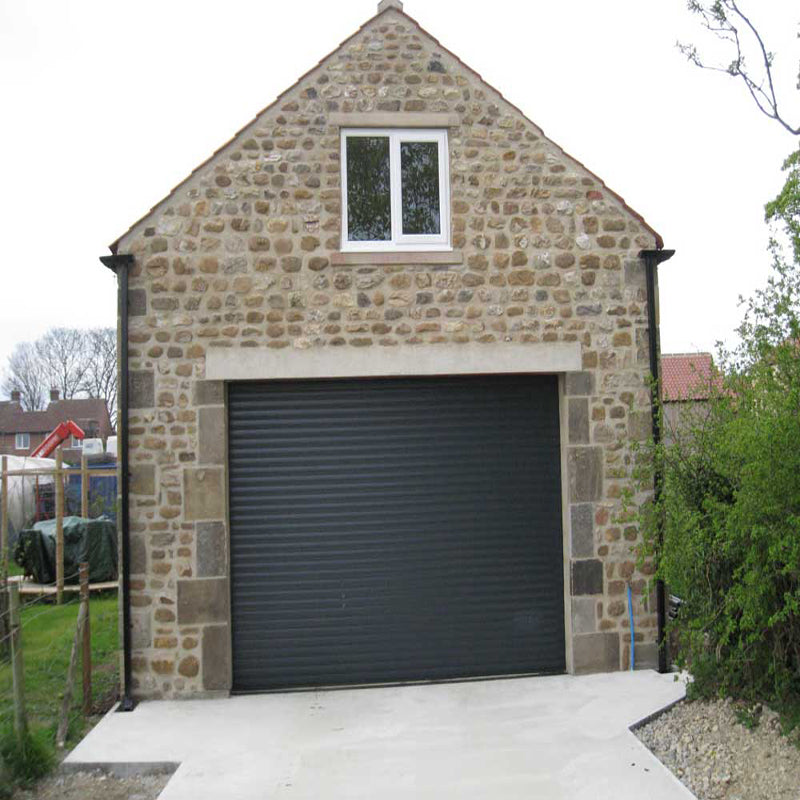 Black metal roller shutter door installed on a stone garage building.